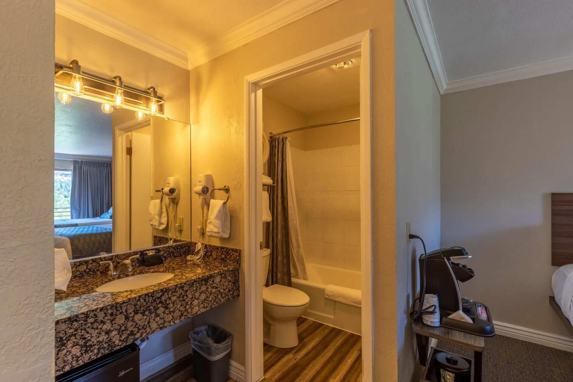 A hotel bathroom with a granite vanity, mirror, toilet, and tiled shower.