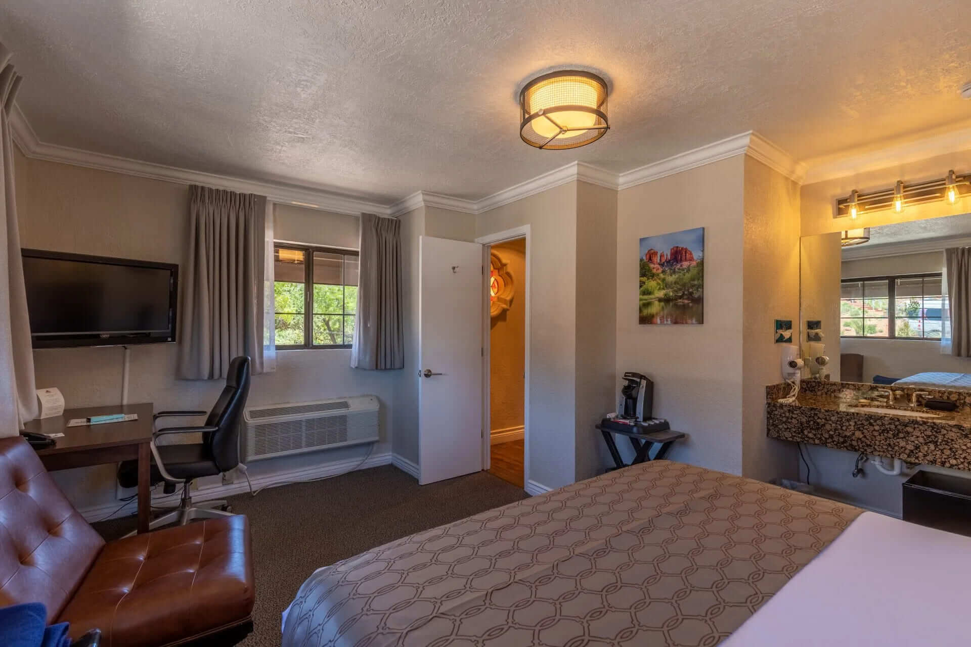 A hotel room with a bed, desk, TV, and bathroom