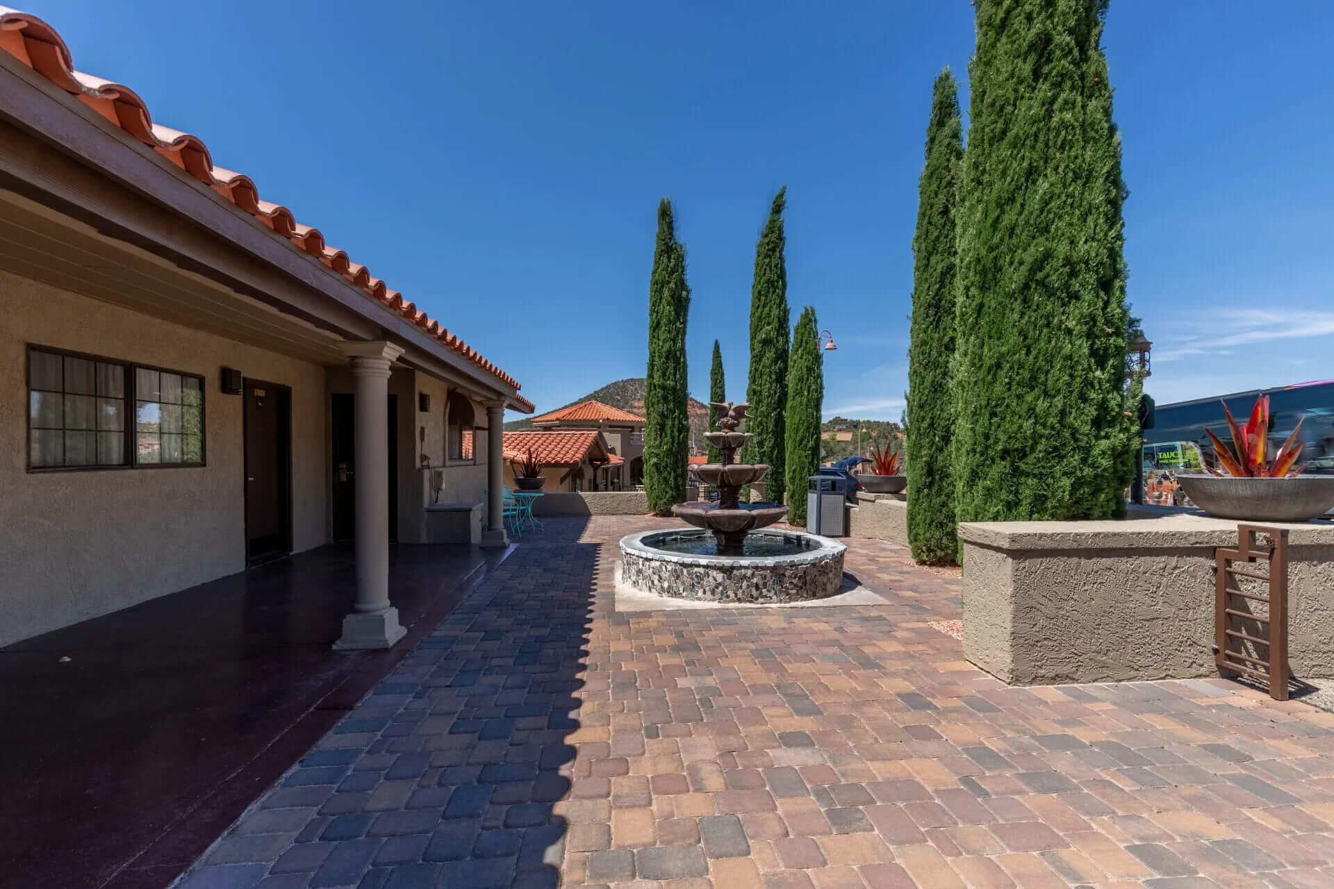 A courtyard with a fountain, trees, and a building with a terracotta roof